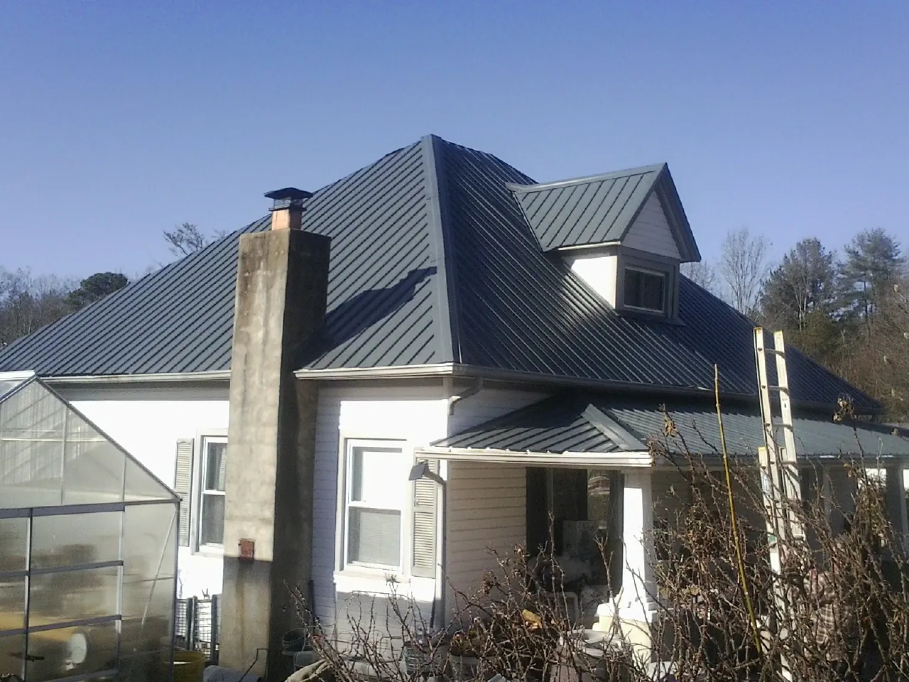 Dark blue standing seam metal roof on a white farmhouse with dormer — Slate & Tile Roof Repair by Roofing Brothers in Copemish