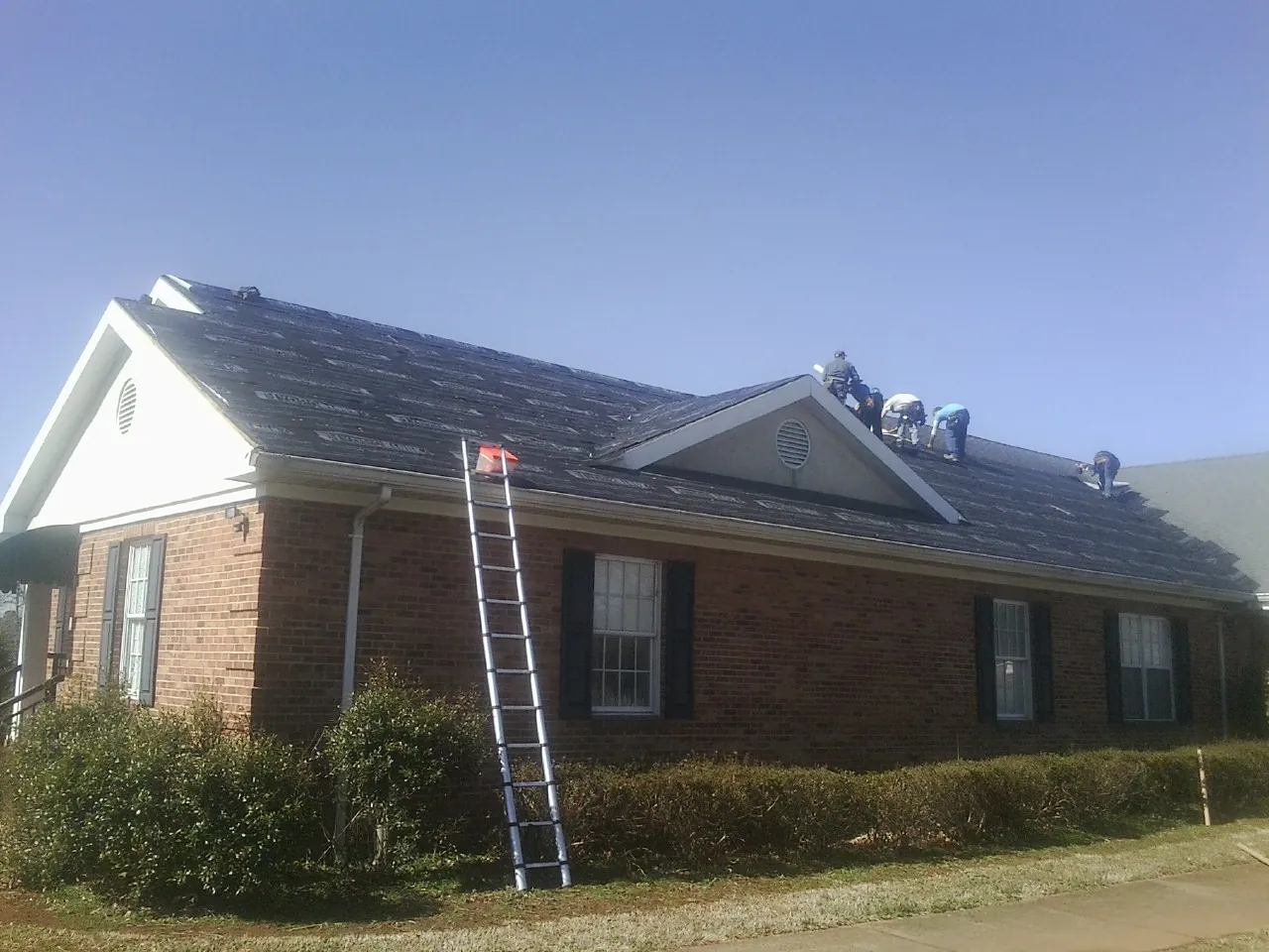 Crew tearing shingles off a brick ranch roof with a ladder set — Emergency Roof Repair work by our crew in Copemish