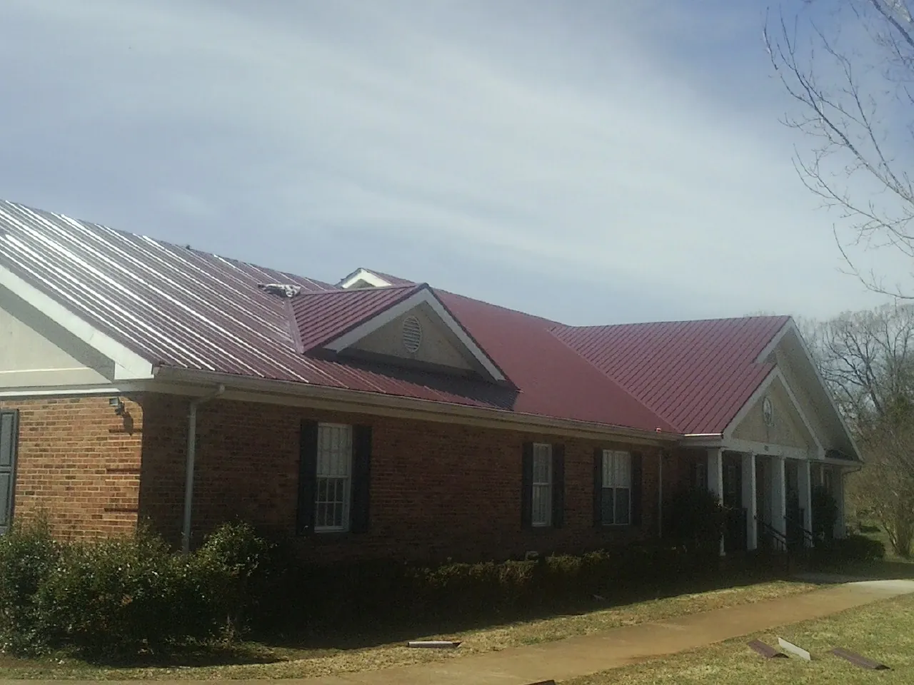 Red metal roof with gabled entries on a long brick building, from a Hail Damage Roof Repair job in Copemish