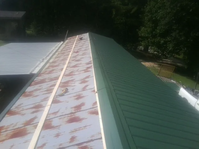Old rusted panels beside newly installed green metal roofing — Wind Damage Roof Repair by Roofing Brothers in Copemish