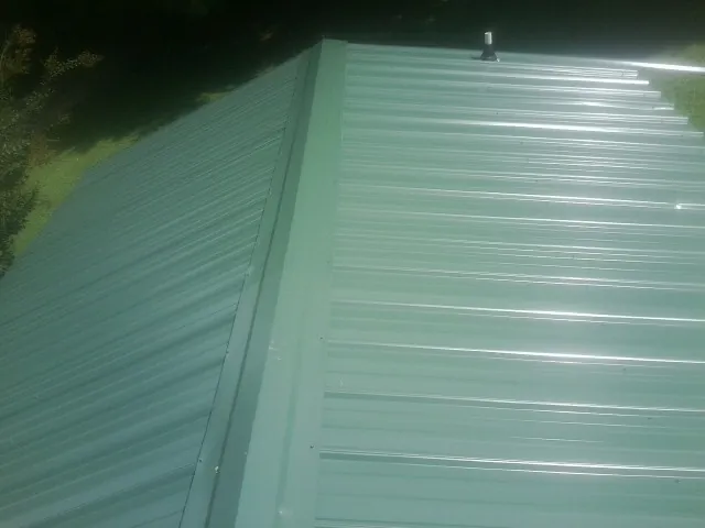 New green metal panels meeting at the ridge of a roof — Flat Roof Repair work by our crew in Copemish