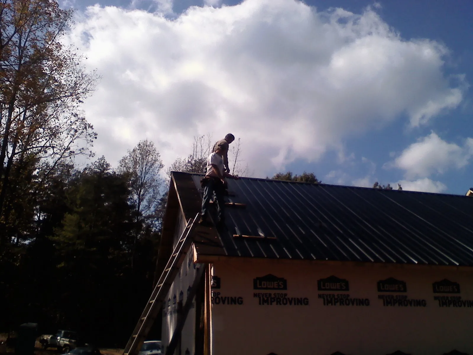 Roofer fastening dark metal panels high against a cloudy sky, from a Roof Inspection job in Copemish
