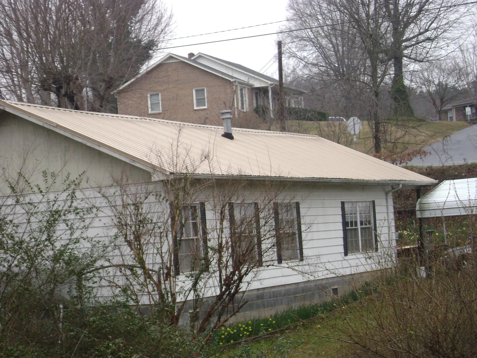 Tan metal roof on a white sided house set into a hillside — Commercial Roofing by Roofing Brothers in Copemish