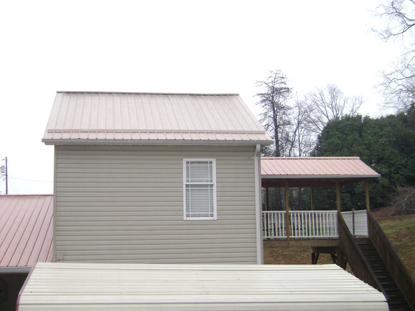Tan metal roofs on a two story addition and attached porch, from a Roof Replacement job in Copemish