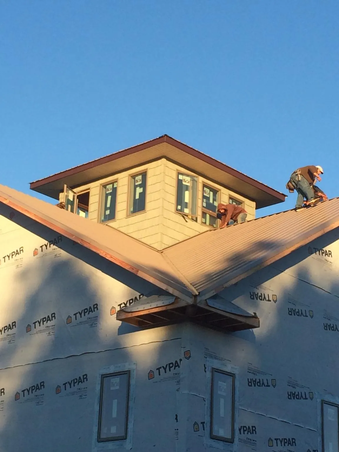 Roofers working around a rooftop cupola on a new metal roof at sunset — Roof Waterproofing in Copemish by Roofing Brothers